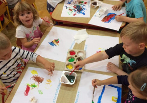 Grupa maluchów maluje farbami na kartkach papieru